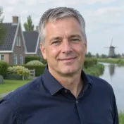 Man van middelbare leeftijd met kort grijzend haar en een donkerblauw overhemd glimlacht vriendelijk