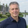 Man van middelbare leeftijd met kort grijzend haar en een donkerblauw overhemd glimlacht vriendelijk